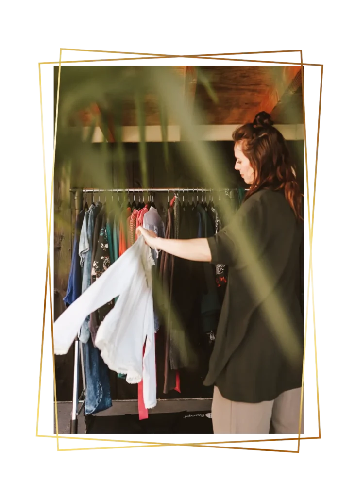 Stylist pakt een wit kledingstuk van een kledingrek met verschillende items.